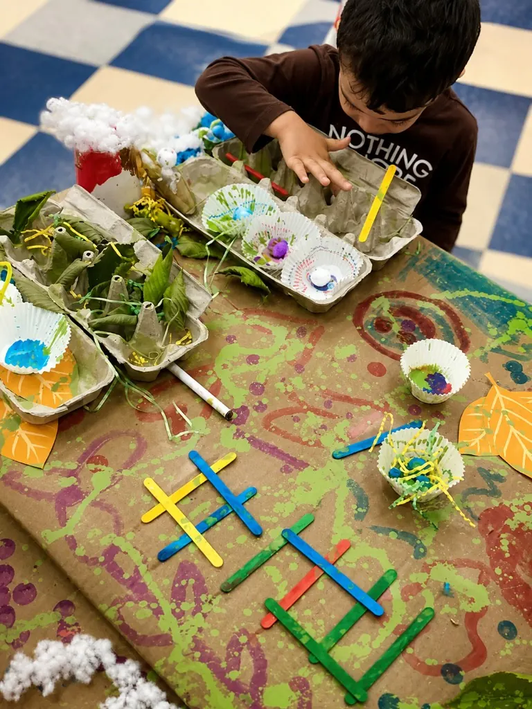 A child building a nature collage from egg cartons, leaves, and craft sticks