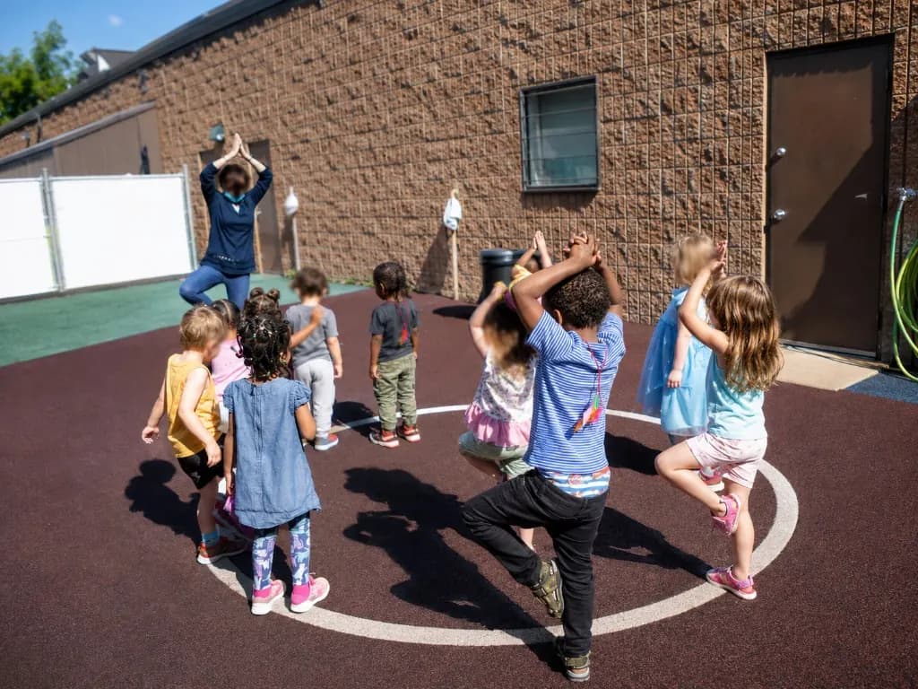 An educator leading children in outdoor yoga and stretching on the play surface