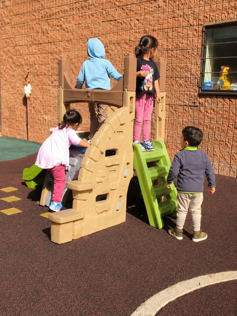 Children taking turns on the outdoor climber in the fenced play area