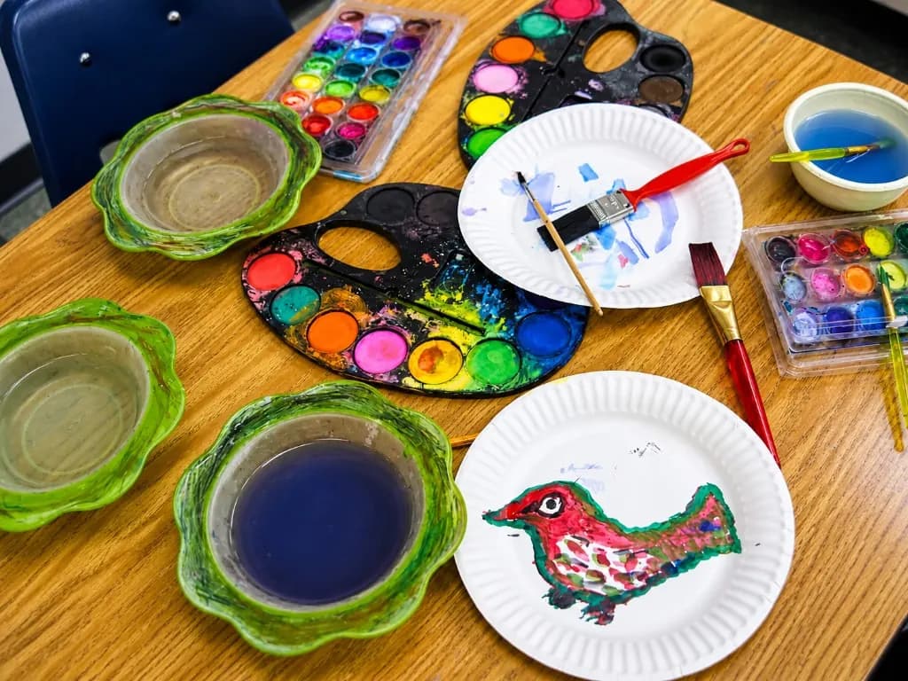 Watercolour palettes, brushes, and a child’s painting of a bird on a paper plate