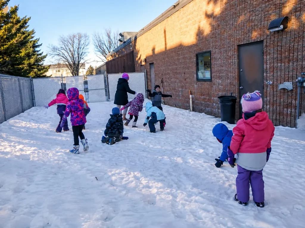 Children playing in the snow in the fenced outdoor area on a bright winter day